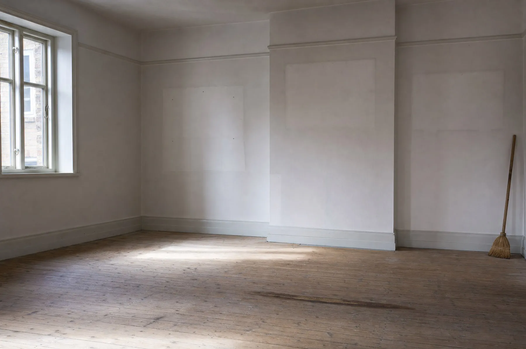 Ein leergeräumtes Zimmer mit gefegtem Boden, an der Wand lehnt ein Besen.